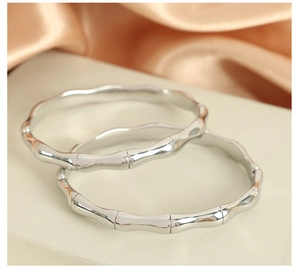 Close-up of two silver bamboo-style bangles on silk, detailing metal texture and knots