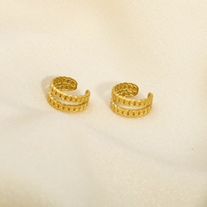 Macro shot of gold double-row chain ear cuffs on soft beige fabric background
