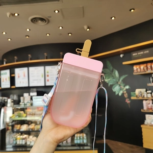 Pink popsicle-shaped plastic cup with colorful strap held in a cafe setting