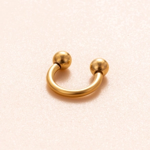 Macro shot of golden horseshoe circular barbell with spherical screw ends on pink background