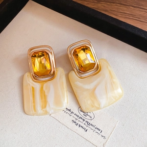 Macro detail of square resin earring with marble texture and inset yellow crystal