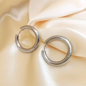 Detailed close-up of polished silver titanium steel hoop earrings on silk background