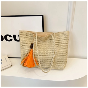 Detail of a beige woven straw tote bag with vibrant orange tassel pendant and texture