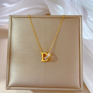 Close-up of a gold D-letter and crystal ring pendant on a white silk background