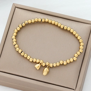 Detailansicht eines goldenen Perlenarmbandes mit zwei Glockenanhängern auf Box