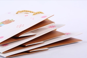 Detail of stacked cartoon bear gift bags with golden woven handles and pink flower accents