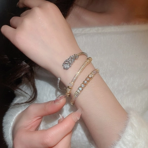 Detail of layered gold-plated bracelets with zircon inlays on a white sweater sleeve