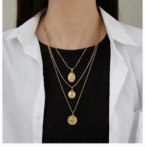 Detailed close-up of layered 18K gold-plated titanium necklaces with coin pendants on model