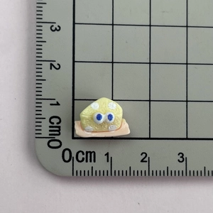 Detailed macro view of 1cm cartoon cheese resin charm with ruler for scale
