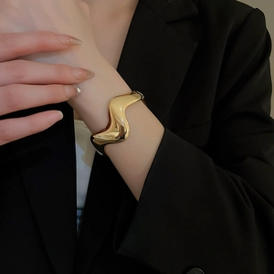 Close-up of a wide golden wavy bangle with a polished mirror finish on a model's wrist