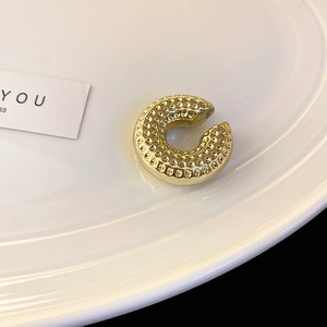 Détail d'un ear cuff doré en forme de C avec finition martelée sur une assiette blanche