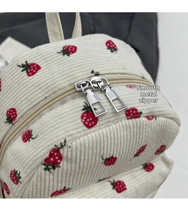 Close-up of smooth silver metal double zippers on beige corduroy strawberry backpack
