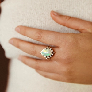 Gros plan d'une bague opale en forme de poire sur monture en argent vieilli portée