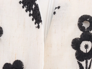 Macro detail of black floral embroidery on cream linen fabric with invisible zipper