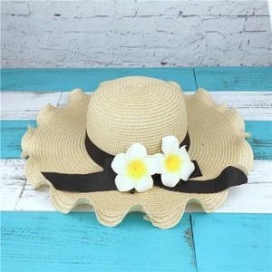 Detail of wide brim straw sun hat with wavy edges and decorative tropical frangipani flowers