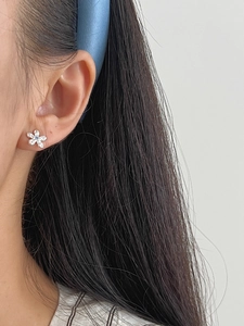 Detailed view of silver flower stud earring with blue gemstone on a female model
