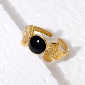 Gold plated stainless steel open ring with black stone and floral accents on marble
