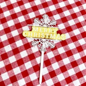 Macro detail of Merry Christmas cake topper with golden text on festive plaid fabric background