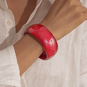Close-up of a wide glossy red acrylic bangle bracelet worn over a white linen sleeve