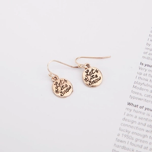 Detail of gold Let it Snow earrings with snowflake engraving on vintage book background