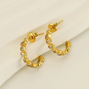 Macro shot of gold-plated C-shape earrings with inlaid zircon on textured background