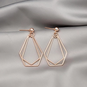 Close-up of geometric double-layer rose gold pentagon drop earrings on silk fabric