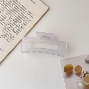 Close-up of a frosted clear square hair claw clip styled with books and lemon water
