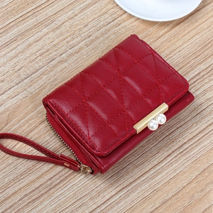 Elegant red quilted short wallet with pearl clasp and wristlet strap on a wood surface