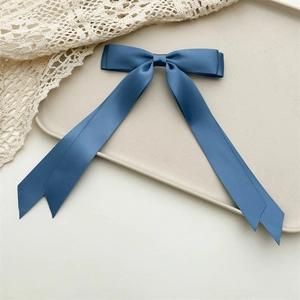 Detailed view of elegant navy blue satin ribbon bow hair clip on a minimalist tray