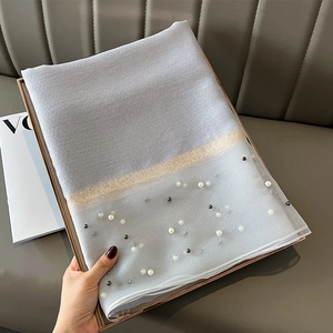 Close-up of light gray silk scarf with white lace trim, gold glitter, and pearl bead accents