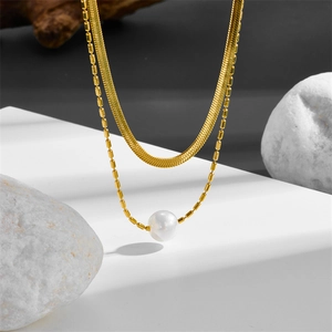 Detail of layered gold snake chain and pearl necklace displayed on artistic stones