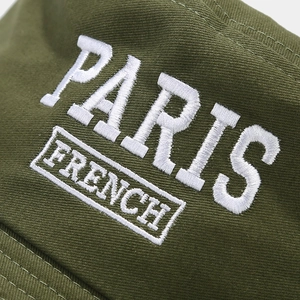 Detailed macro view of white PARIS embroidery on dark green cotton twill bucket hat