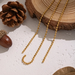 Close-up of golden stainless steel bead chain with pine cones and natural elements