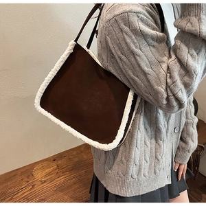 Close-up of brown suede tote bag with white faux fur trim on knit sweater background
