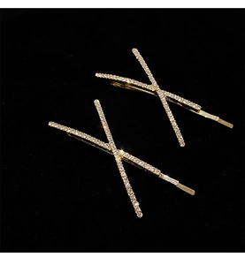 Detail shot of two gold-colored X-shaped hair clips with crystal rhinestones on velvet