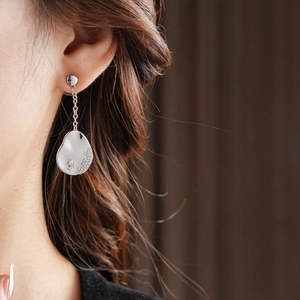 Gros plan de boucles d'oreilles asymétriques goutte d'eau avec émail blanc et zircons