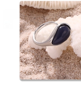 Detailed shot of waterdrop blue resin stone ring on coral background with sand