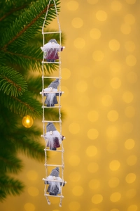 Close-up of four wool felt gnomes on a rope ladder hanging by a Christmas tree