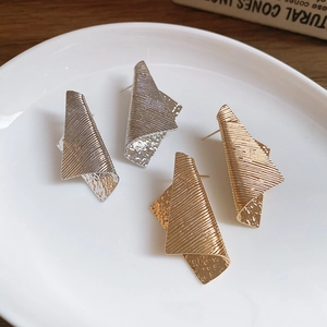 Close-up of gold and silver irregular geometric earrings with brushed metal texture