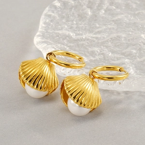Close-up of golden shell-shaped earrings with white pearls on a light gray fabric background