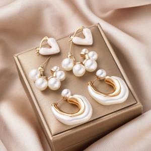 Three-pair earring set with gold hearts and pearls displayed on a luxury jewelry box