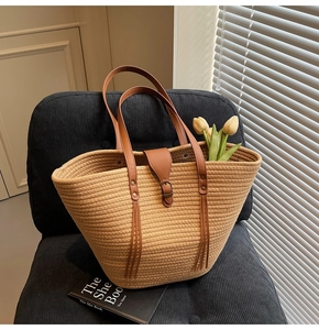 Detail of woven straw tote bag with brown leather handles and decorative flowers