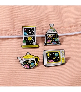 Detail view of space-themed enamel pins featuring a starry teapot and vintage television