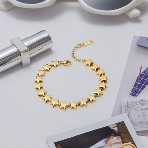 Detail shot of 18K gold star bracelet in a lifestyle setting with fashion accessories