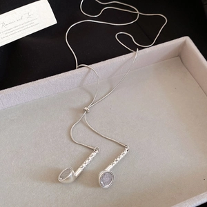 Close-up of silver microphone pendants and snake chain on a gray velvet jewelry tray