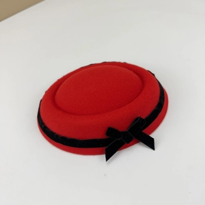 Elegant red wool pillbox hat featuring a black velvet ribbon bow on a clean white background