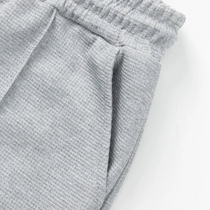 Detalle macro de pantalones de punto gofrado gris claro con cintura elástica y bolsillos laterales
