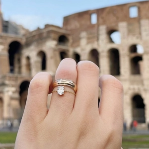 Detail of gold stacked rings with oval gemstone set against blurred Roman background