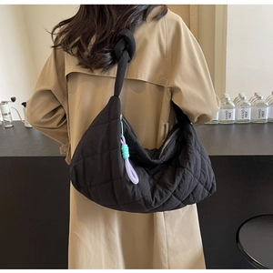Detail of large black quilted tote bag with a knotted strap shown in use on shoulder