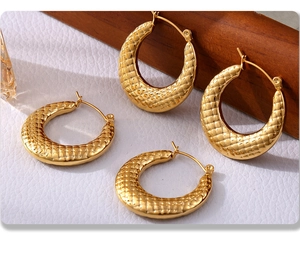 Macro detail of U-shaped gold earrings featuring embossed crocodile texture patterns